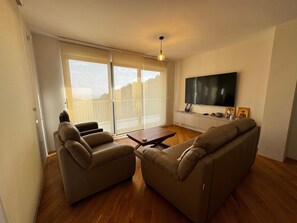 Ett vardagsrum med en soffa, ett soffbord och en tv som är monterad på väggen.