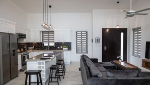 Une cuisine moderne avec un îlot central, des tabourets de bar et un canapé de couleur sombre dans l’espace salon.