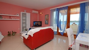 Camera da letto in tonalità rosa con un letto rosso, una televisione e un balcone con tende blu.