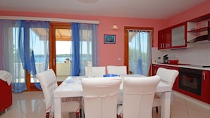 Zona pranzo con tavolo e sedie, cucina con mobili rossi e vista attraverso le porte vetrate.