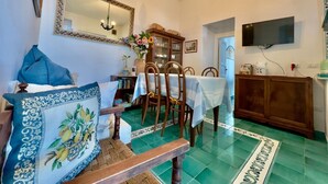 Un coin repas avec une table dressée pour quatre personnes, un banc en bois, un miroir, un lustre et un téléviseur fixé au mur.