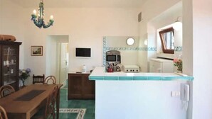 Une cuisine compacte dotée d’un îlot central, d’un coin repas avec une table et des chaises en bois, et d’un lustre.