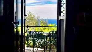 Vista de um quarto com porta para área externa, incluindo mesa, cadeiras, corrimão, céu e vegetação.