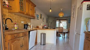 Una cocina con armarios de madera, un lavamanos, un cubo de basura y una zona de comedor con mesa y sillas.