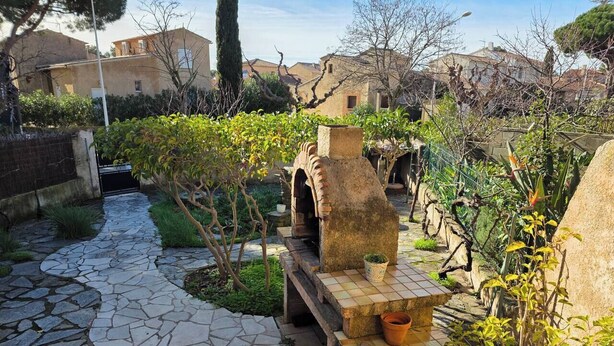 Un sendero de piedra que atraviesa un patio con un banco de azulejos, plantas en macetas y una construcción rústica de piedra.