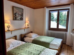 A room with two beds, a wooden ceiling, a window with a view of trees, a radiator, and a wall-mounted picture. - Detached 5-bedroom family chalet in La Rosière-Centre. (Montvalezan)