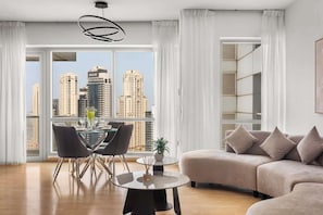 A modern living room with a dining area, large windows with city views, and a sofa. - Modern 2BR Marina Apt | Canal View | Pool & Sauna (Dubai)