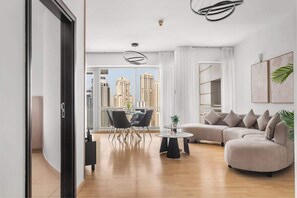 A modern living room with a curved sofa, a dining table, and chairs. There is a large window with a view of tall buildings. - Modern 2BR Marina Apt | Canal View | Pool & Sauna (Dubai)