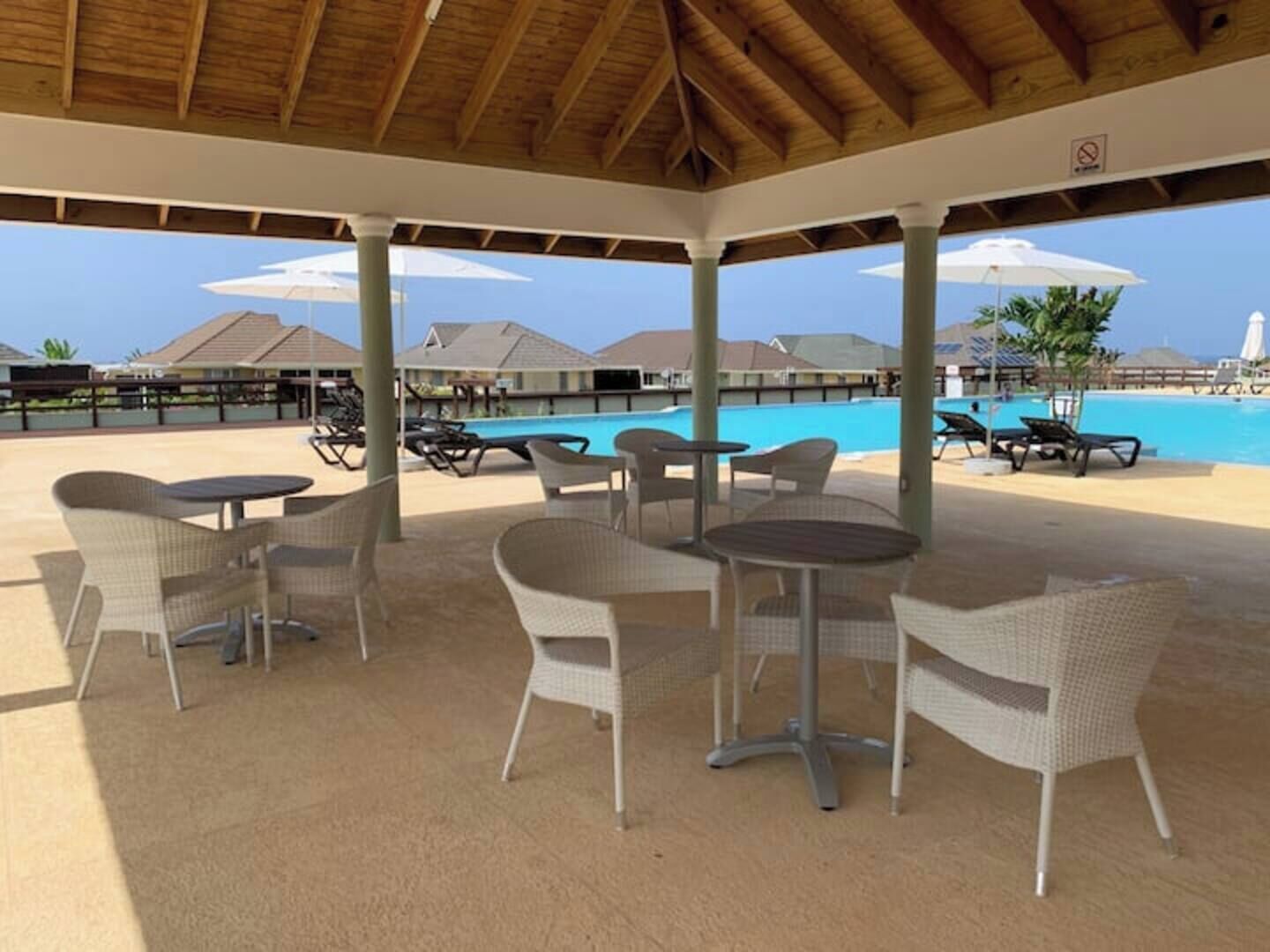 Ein überdachter Außenbereich mit Korbmöbeln und einem Pool im Hintergrund.