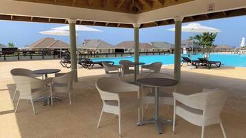 A covered outdoor area with wicker furniture and a pool in the background.
