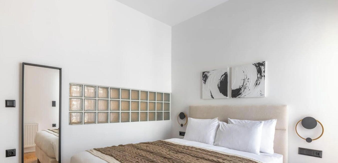 A modern bedroom with a large bed, a mirror, and abstract wall art.