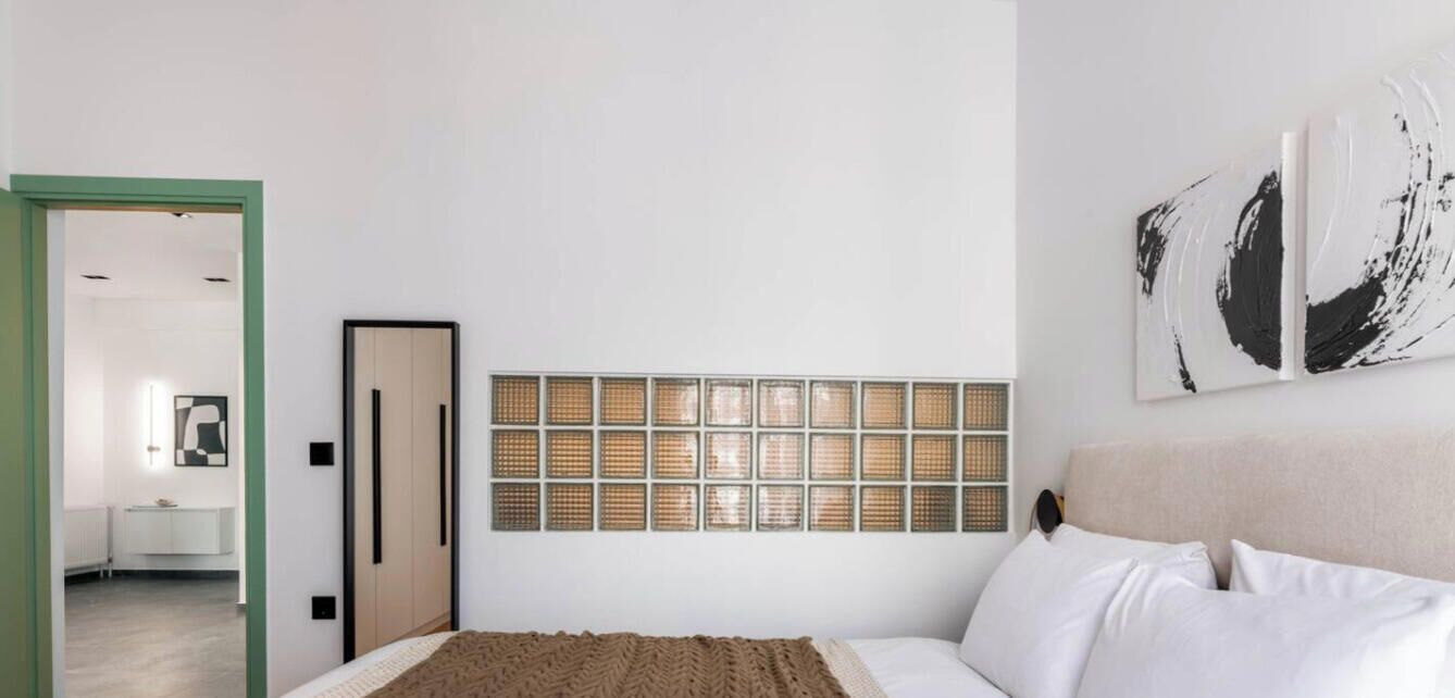 Une chambre à coucher avec un lit, une œuvre d’art accrochée au mur, une porte et une fenêtre.