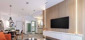 A modern living room with a flat-screen TV mounted on a wooden panel wall, a dining area with a table and chairs, and a kitchen with a countertop and cabinets. - Sunlit Balcony | Family APT | Whirpool & Netflix (Kallithea)