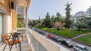 Ein Balkon mit Tisch und Stühlen, der auf eine Straße mit parkenden Autos und Bäumen blickt.