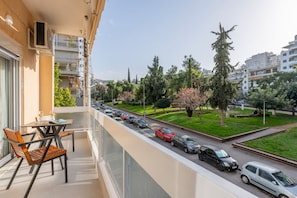 Ein Balkon mit Tisch und Stühlen, der auf eine Straße mit parkenden Autos und Bäumen blickt.