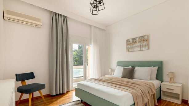 Ein Schlafzimmer mit Bett, Sessel, Nachttisch, Lampe und einem Bild an der Wand.