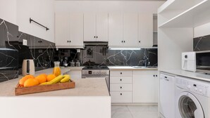Eine moderne Küche mit weißen Schränken, einer Marmor-Spritzschutzleiste, einem Einbauofen und einer Waschmaschine.