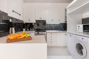 Eine moderne Küche mit weißen Schränken, einer Marmor-Spritzschutzleiste, einem Einbauofen und einer Waschmaschine.