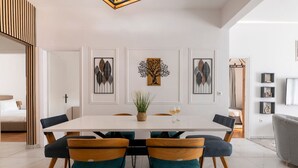Ein moderner Essbereich mit einem weißen Tisch, blaugrünen Stühlen und gerahmten Kunstwerken an der Wand.