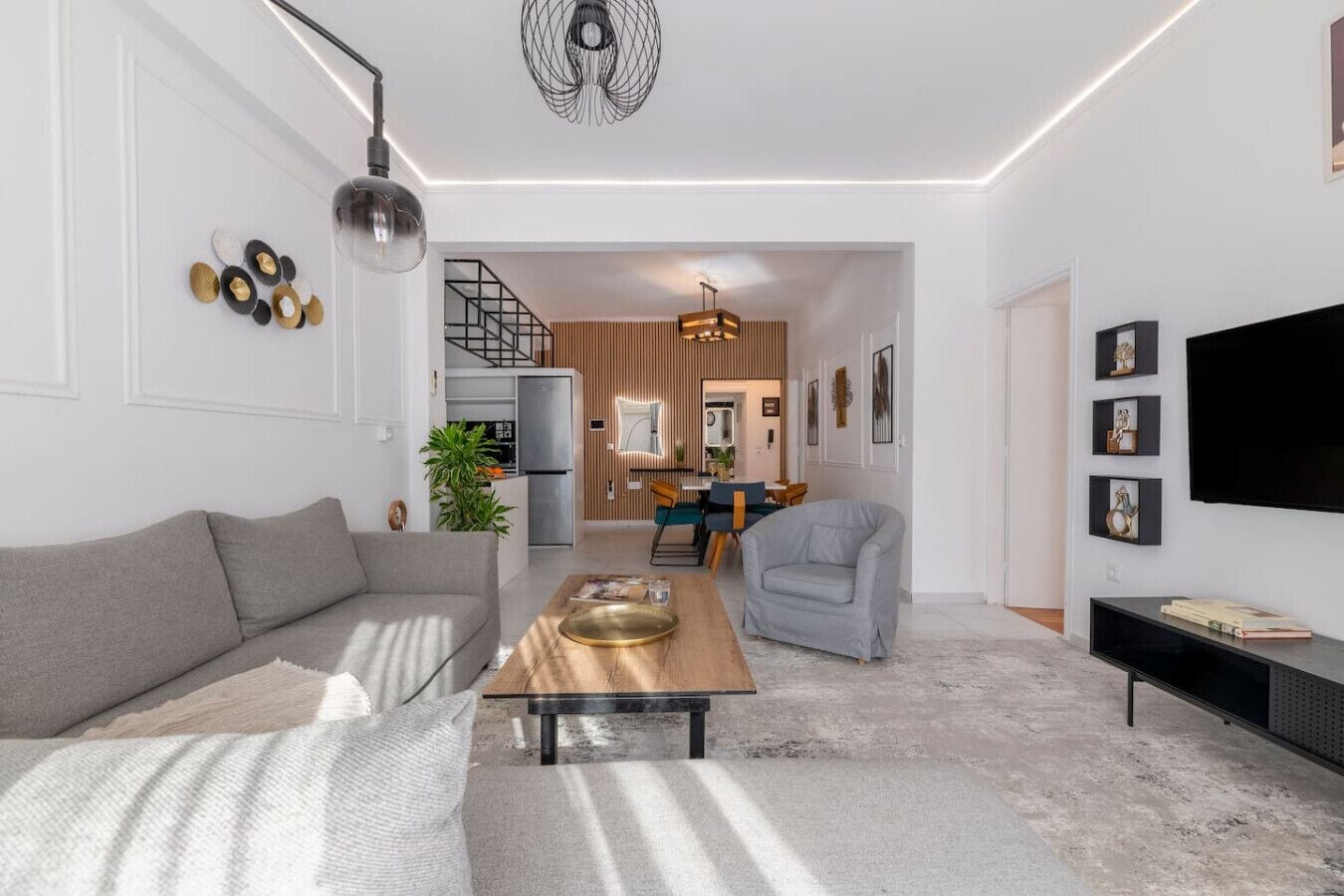 A modern living room with a sofa, a coffee table, a TV, and a staircase leading to a kitchen.