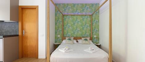 A four-poster bed with a leaf-patterned wallpaper, a wooden door, and a small bedside table.