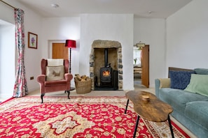Ein gemütliches Wohnzimmer mit Kamin aus Stein, einem roten Teppich mit Muster, einem bequemen Sessel und einem blauen Sofa.