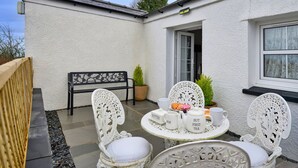 Una casa bianca con tetto nero, un piccolo giardino e un tavolo apparecchiato con tè e burro.