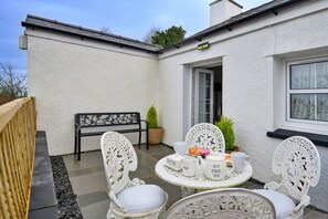 Ein weißes Haus mit schwarzem Dach, ein kleiner Garten und ein Tisch gedeckt mit Tee und Butter.