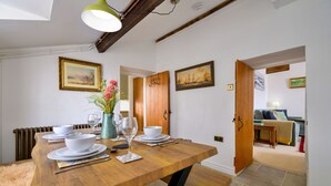 Un'area pranzo con un tavolo in legno apparecchiato per quattro persone, un vaso con fiori e due quadri appesi al muro.