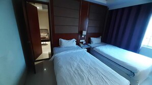 A hotel room with two single beds, a wooden headboard, a bedside table with a lamp, and a window with curtains. - BluBay Waterfront Inani (Cox's Bazar)