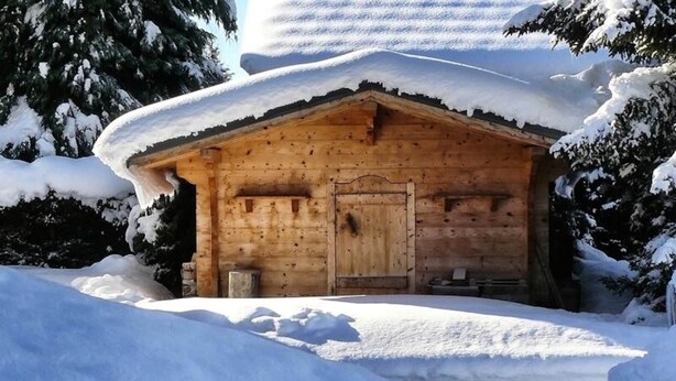 Una baita di legno con tetto imbiancato dalla neve, circondata da alberi.