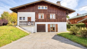 Una casa a due piani in legno con un balcone, un'entrata principale e un vialetto sterrato.