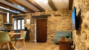 Un interno rustico con pareti in pietra, un tavolo da pranzo in legno con sedie, un divano e un televisore montato a parete.