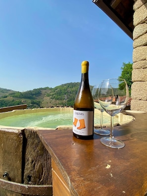 A bottle of wine and a glass on a wooden table with a scenic view of hills and a hot spring in the background.