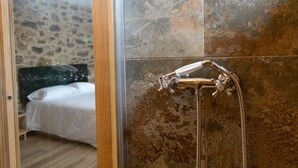 Un bagno con doccia, un letto con biancheria bianca e una parete in pietra.