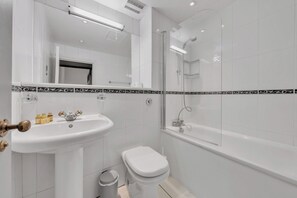 A modern bathroom with a white sink, toilet, and glass-enclosed shower. - Designer Mayfair Apartment (London)