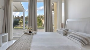 Un dormitorio con cama, cortinas, una bandeja con una copa de vino y vistas al exterior.