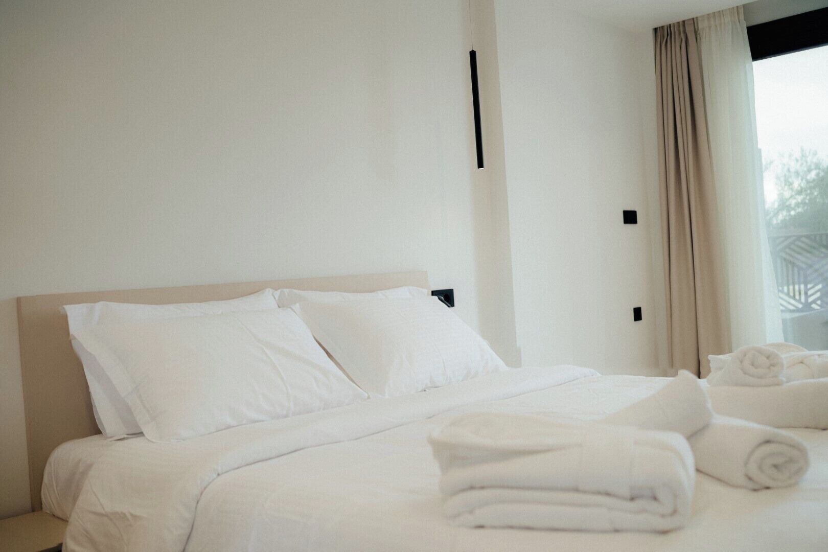 Una habitación de hotel con cama, almohadas y toallas dobladas cuidadosamente.