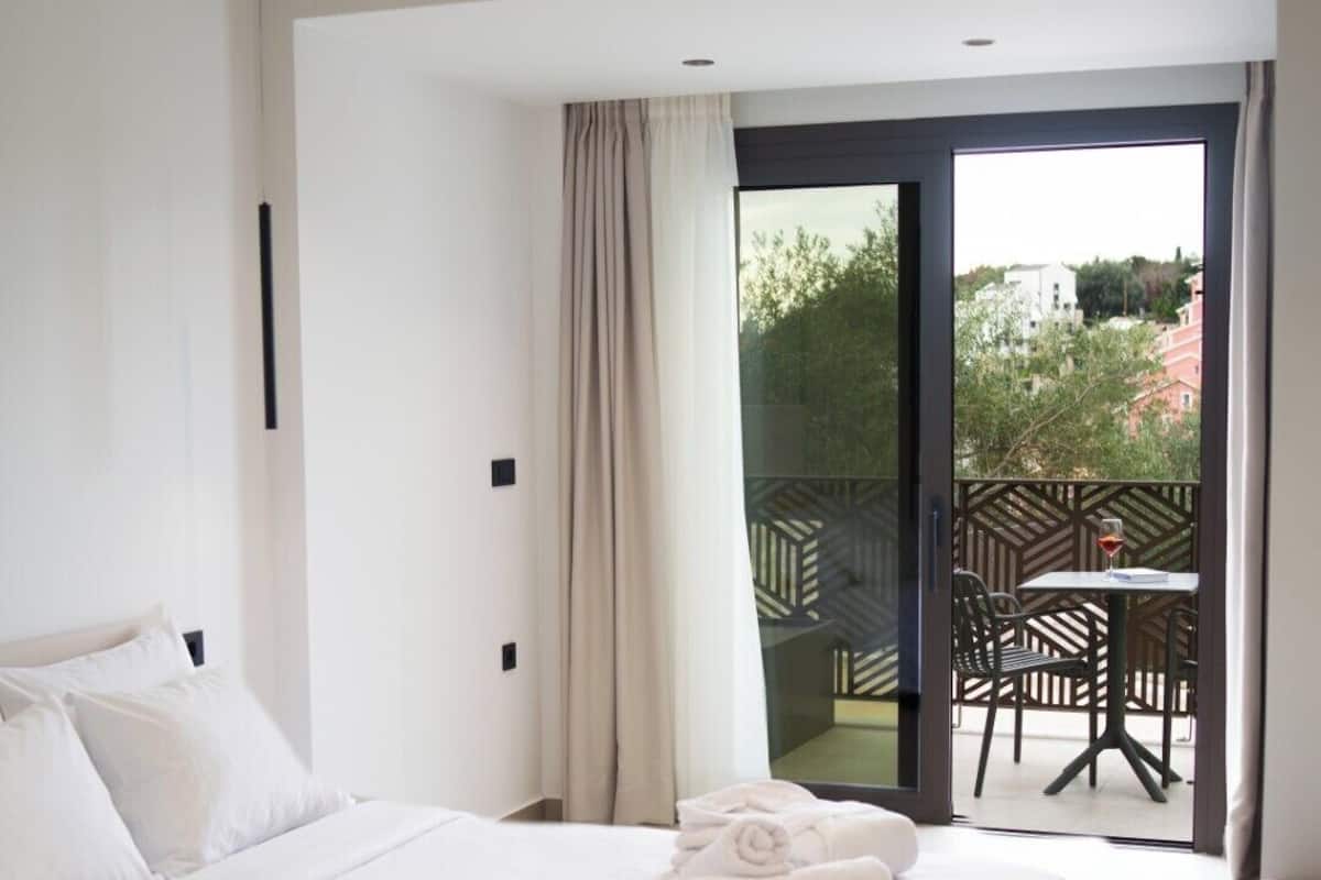 Habitación de hotel moderna con una cama grande, un balcón con mobiliario exterior y vistas del entorno.