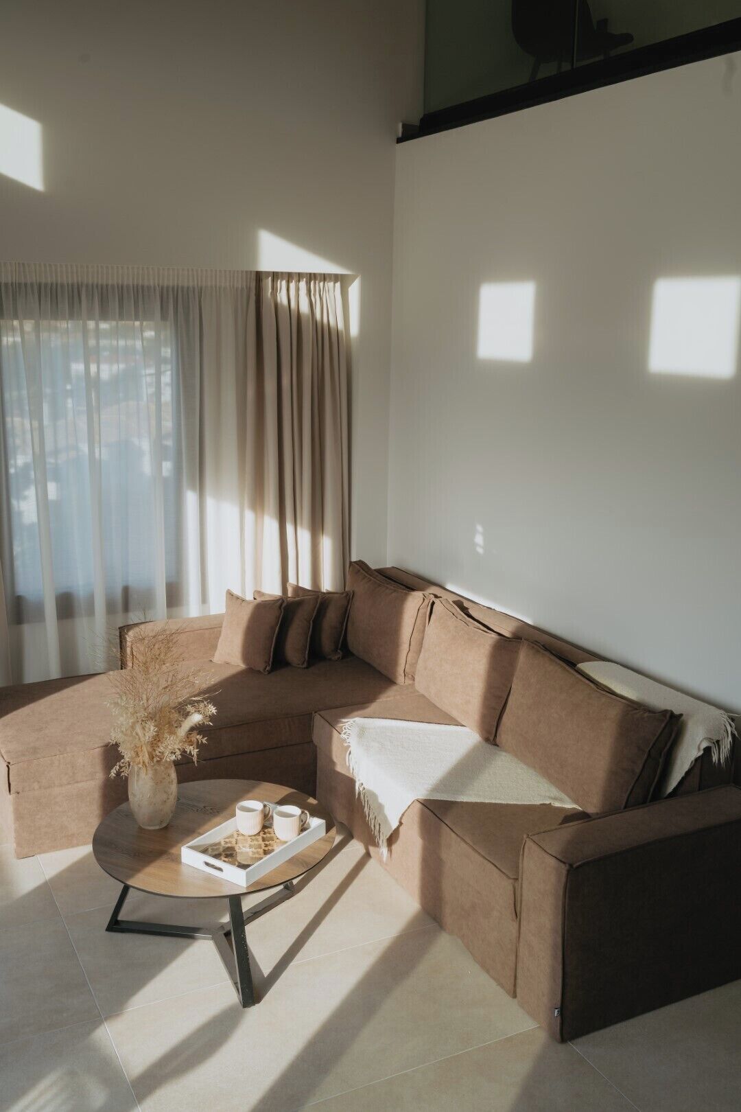 Ein modernes Wohnzimmer mit einem Ecksofa, einem Couchtisch und einer Vase mit Trockenpflanzen.