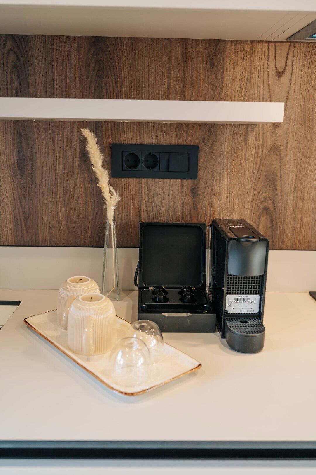 A kitchen counter with a coffee maker, a glass vase with pampas grass, and two white candle holders on a tray.
