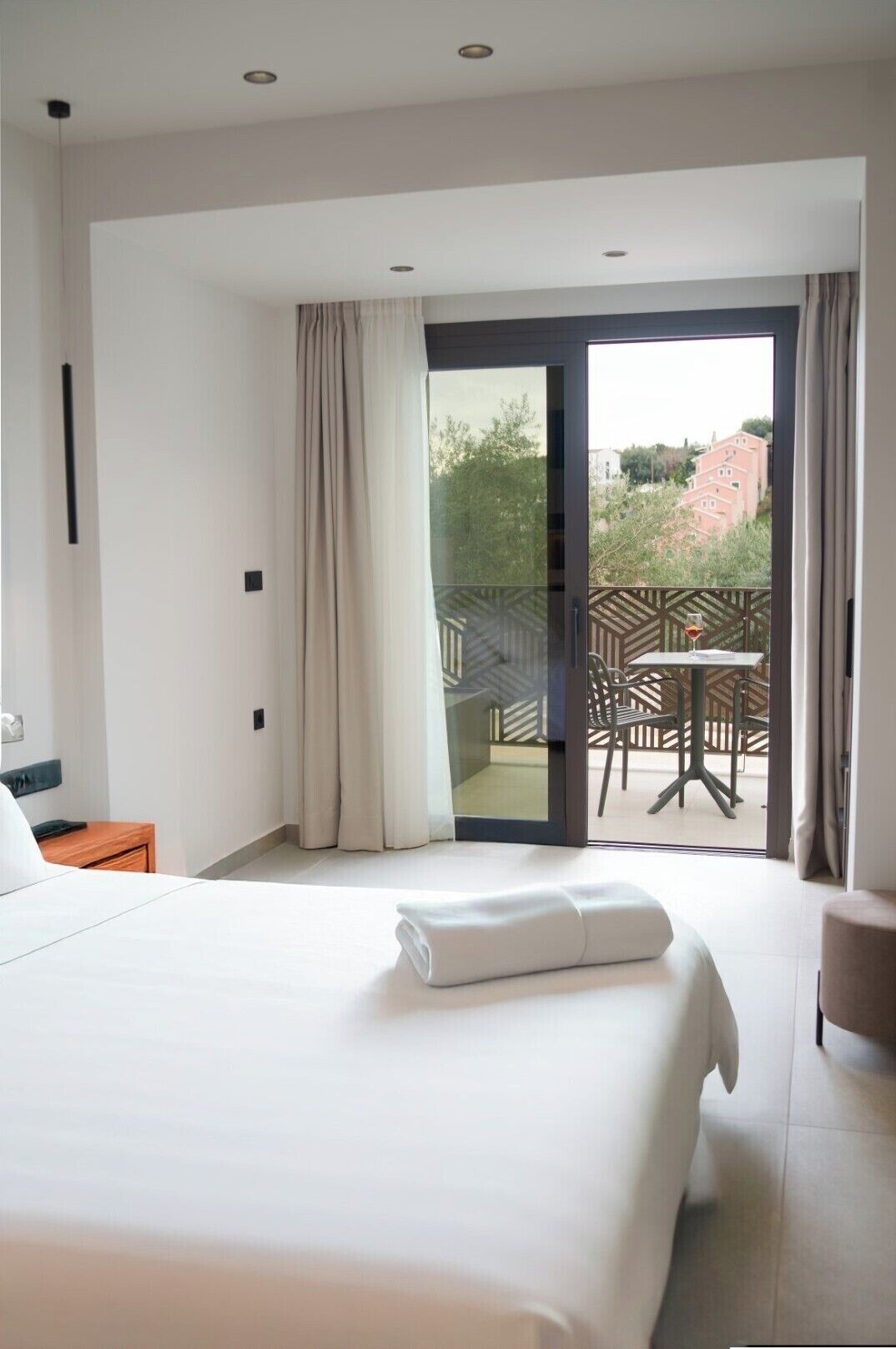 Ein Hotelzimmer mit Bett, einem kleinen Tisch mit einem Weinglas und einem Balkon mit Tisch und Stühlen.