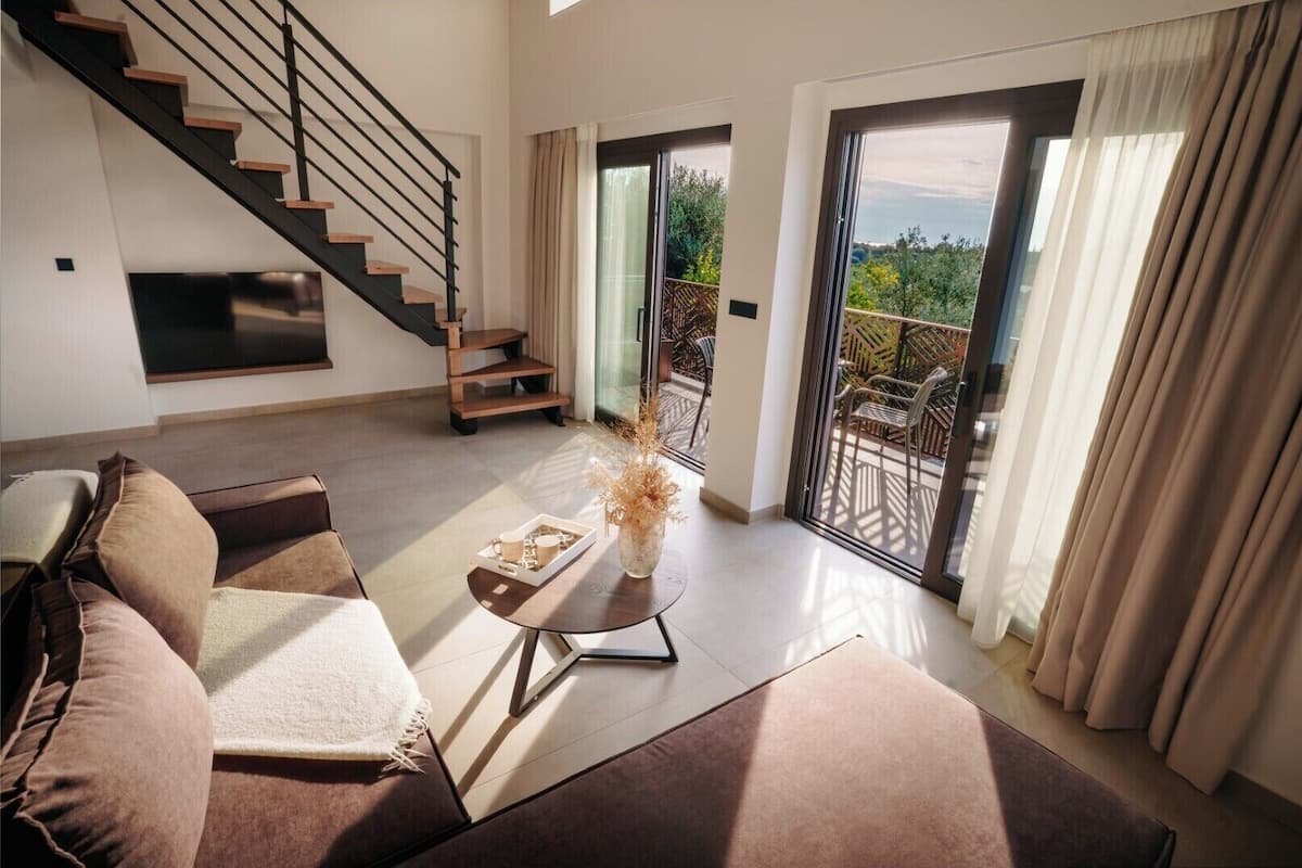 Una sala de estar moderna con una escalera, un sofá, una mesa de centro y vistas al exterior.