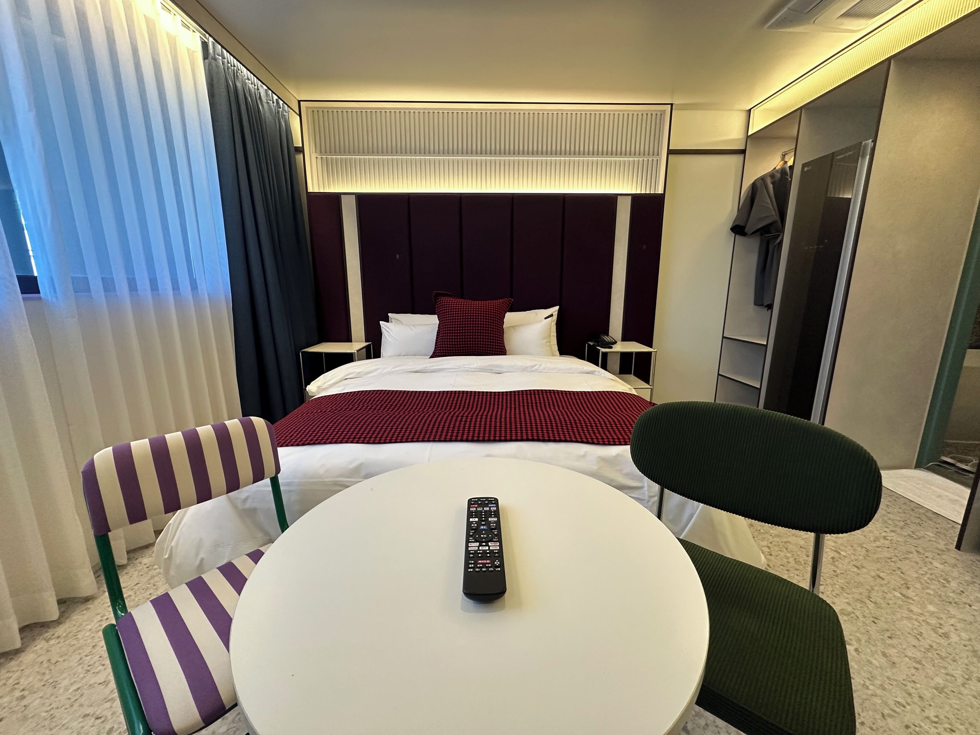 A hotel room with a bed, a round table, two chairs, a TV, and a phone on a bedside table.