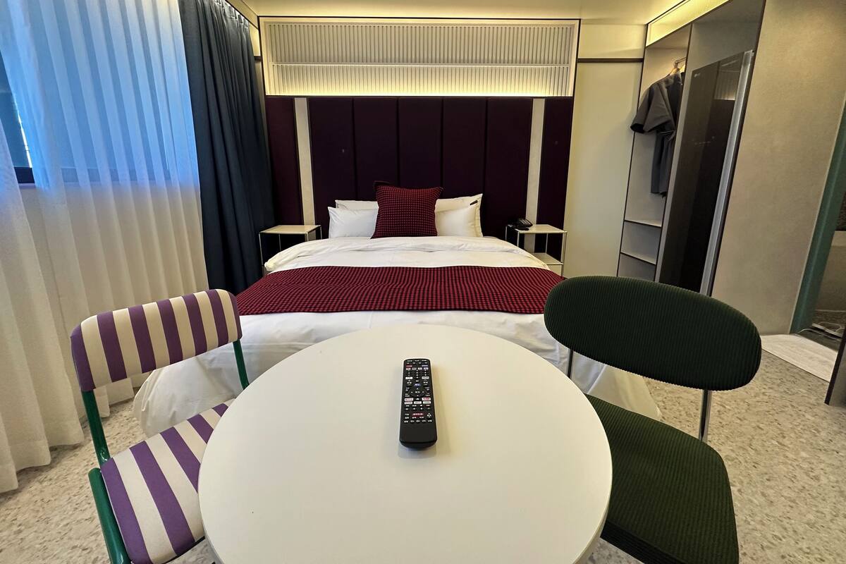 A hotel room with a bed, a round table, two chairs, a TV, and a phone on a bedside table.