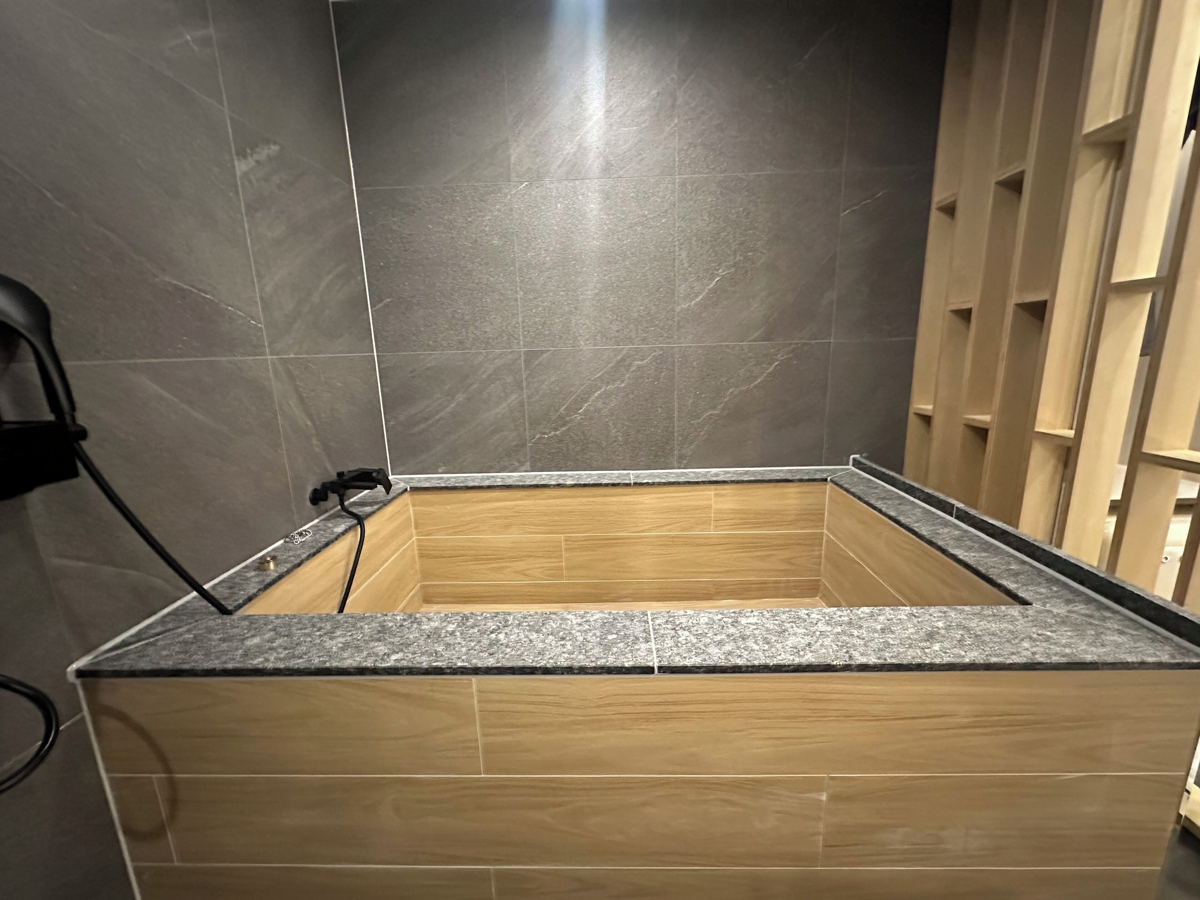 Een badkamer met donkere betegelde wanden, houten kastjes en een granieten aanrechtblad.