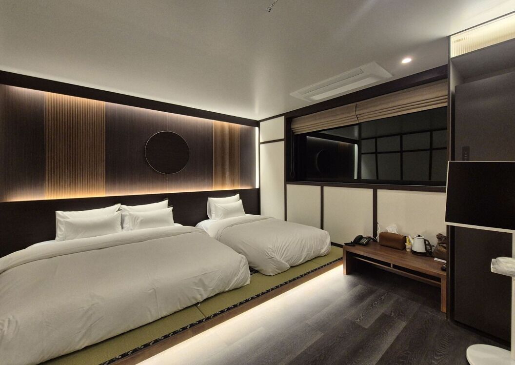 A modern hotel room with two beds, a large window, and a built-in wardrobe.