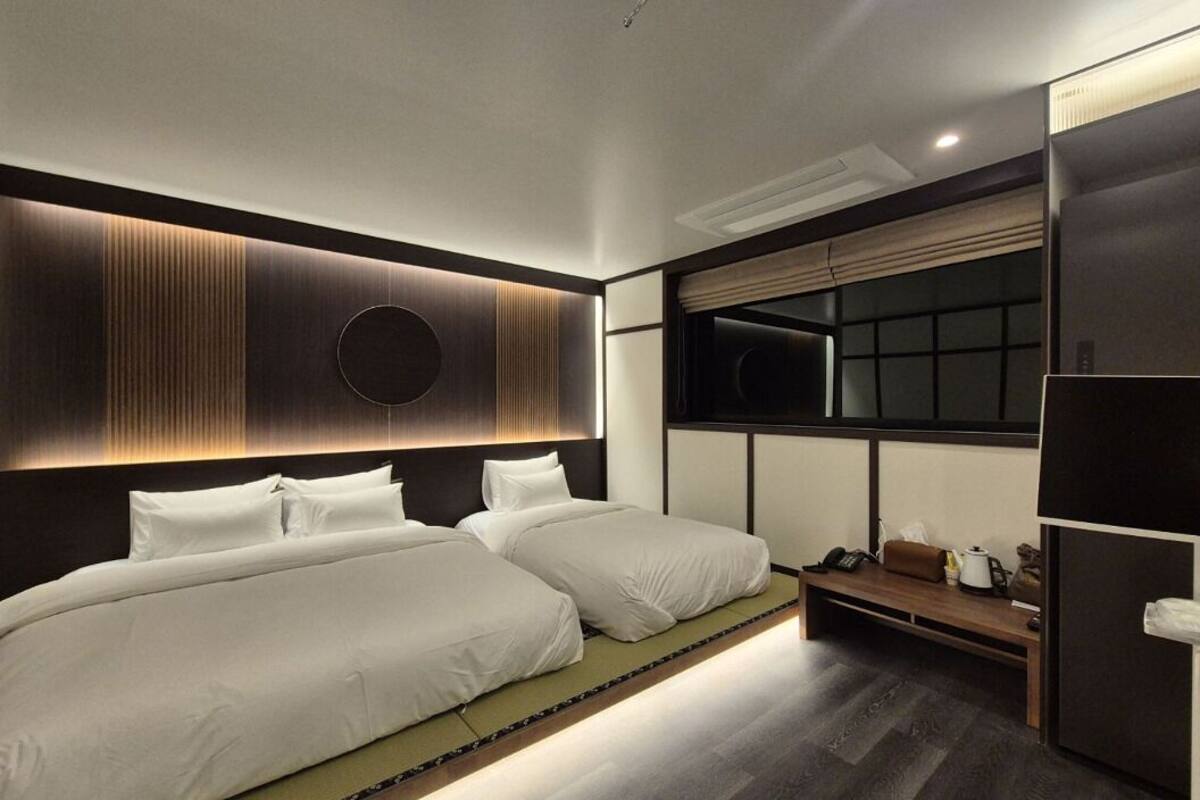 A modern hotel room with two beds, a large window, and a built-in wardrobe.