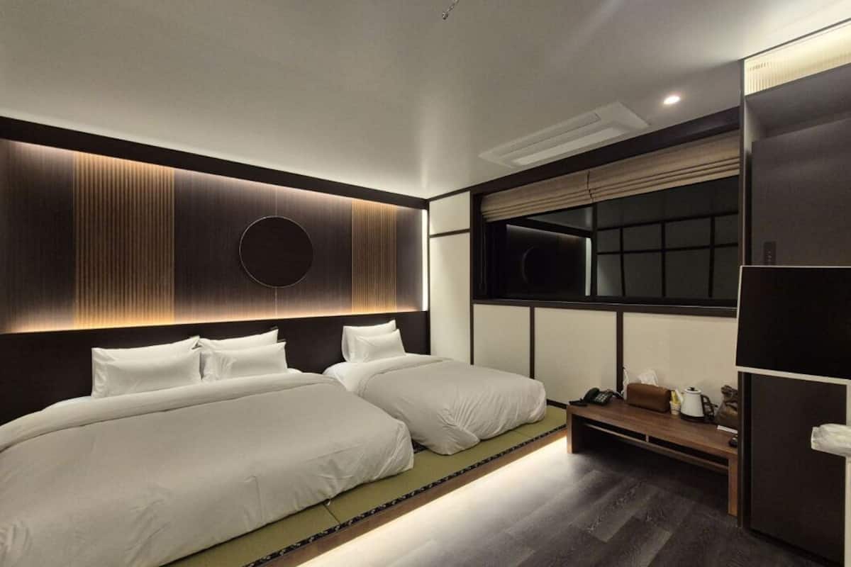 A modern hotel room with two beds, a large window, and a built-in wardrobe.