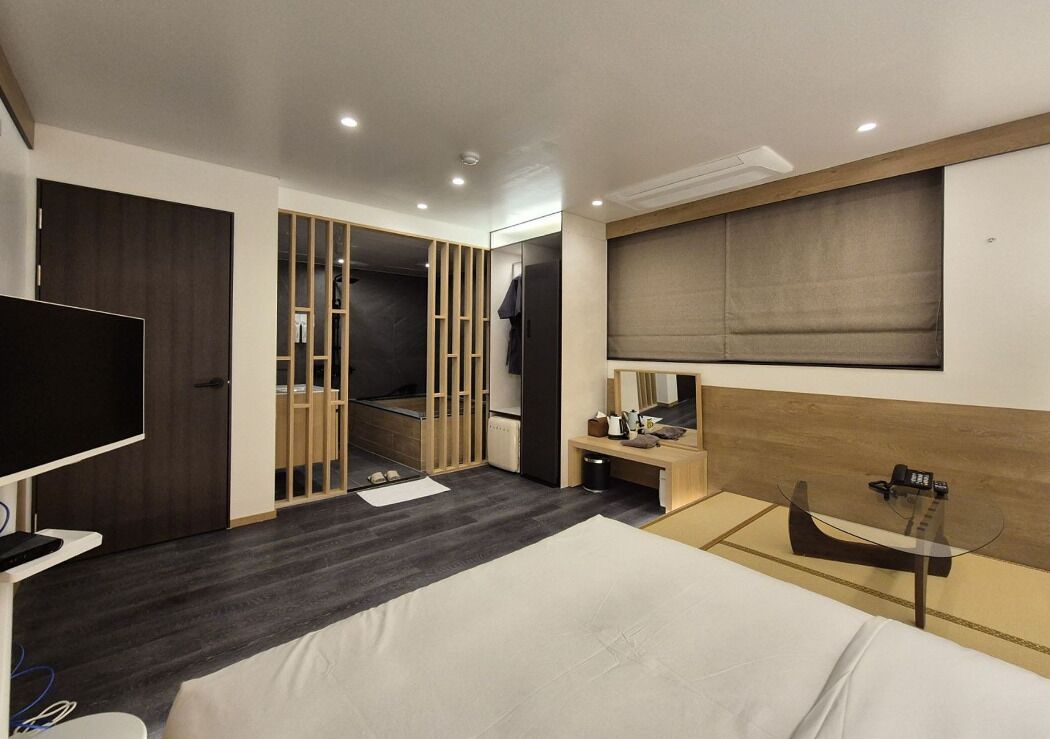 A modern hotel room with a large bed, a TV, a desk, and a walk-in closet.